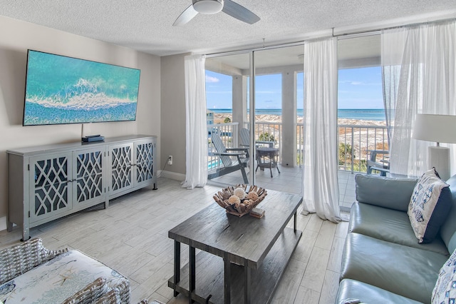 living room featuring a textured ceiling, ceiling fan, a wealth of natural light, and a water view