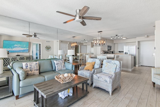 living room featuring a textured ceiling, light hardwood / wood-style flooring, and ceiling fan with notable chandelier