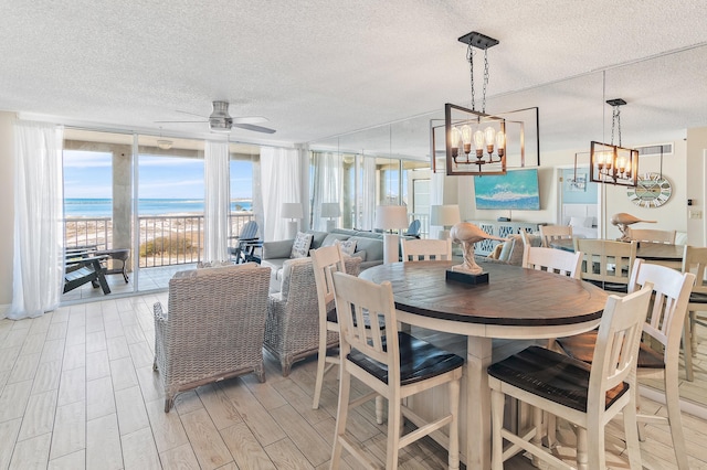 dining room with ceiling fan with notable chandelier, a textured ceiling, a wall of windows, and a water view