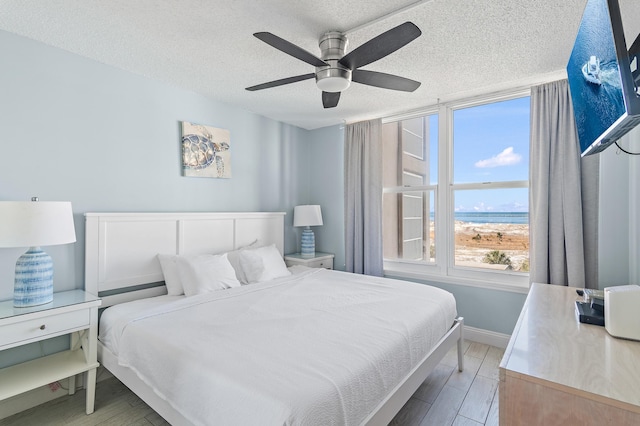 bedroom featuring ceiling fan, a water view, and a textured ceiling