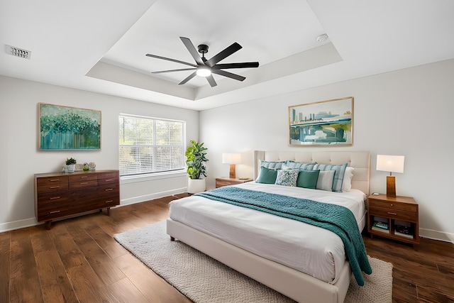 bedroom featuring ceiling fan, a tray ceiling, and dark hardwood / wood-style flooring