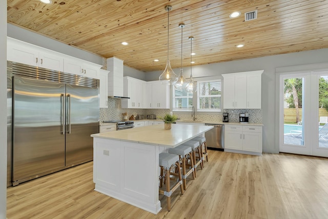 kitchen featuring wooden ceiling, hanging light fixtures, high quality appliances, a kitchen island, and wall chimney range hood