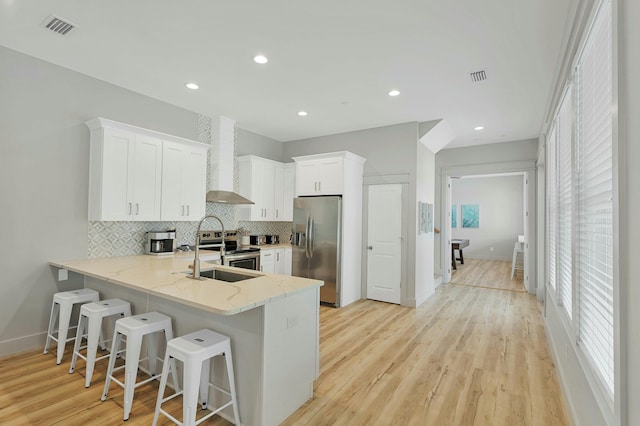 kitchen featuring stainless steel appliances, sink, white cabinets, wall chimney exhaust hood, and a breakfast bar area