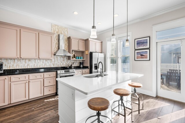 kitchen with hanging light fixtures, a kitchen island with sink, stainless steel appliances, light brown cabinets, and wall chimney exhaust hood