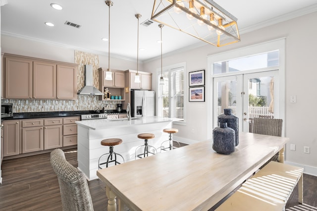 kitchen with hanging light fixtures, appliances with stainless steel finishes, a kitchen island with sink, and wall chimney exhaust hood