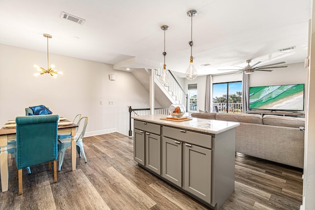 kitchen with gray cabinetry, decorative light fixtures, a kitchen island, ceiling fan with notable chandelier, and dark hardwood / wood-style floors