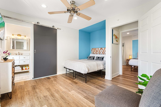 bedroom with ceiling fan, sink, a barn door, and light wood-type flooring