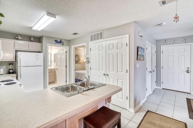 kitchen with white appliances, a kitchen breakfast bar, a textured ceiling, sink, and light tile patterned flooring