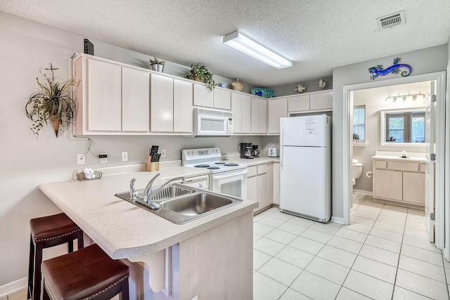 kitchen featuring white appliances, a textured ceiling, a kitchen bar, white cabinets, and sink