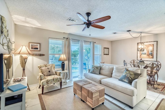 living room with a textured ceiling, ceiling fan with notable chandelier, and light tile patterned floors