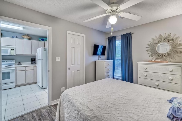 bedroom with a textured ceiling, ceiling fan, white fridge, and light wood-type flooring