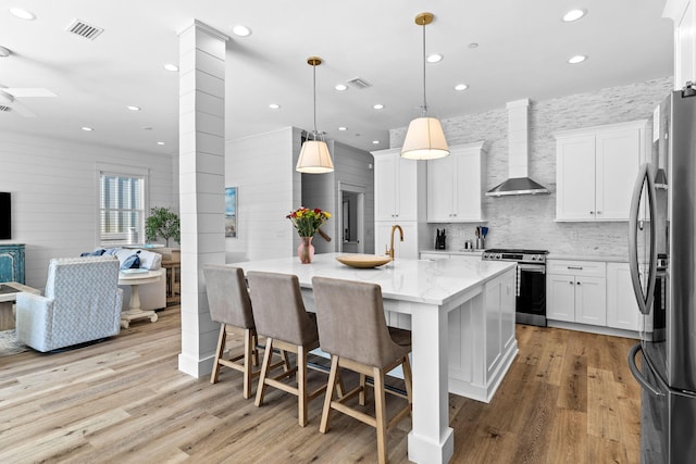 kitchen with stainless steel appliances, wall chimney range hood, white cabinets, and a kitchen breakfast bar