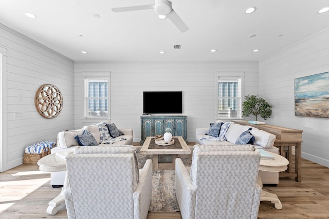 living room with ceiling fan, light hardwood / wood-style flooring, and wood walls