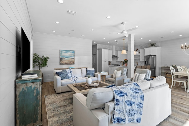 living room with ceiling fan with notable chandelier and light wood-type flooring