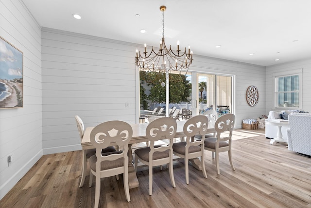 dining space featuring crown molding, wooden walls, light hardwood / wood-style flooring, and a chandelier