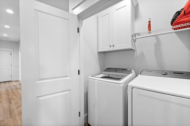 washroom featuring washing machine and dryer, cabinets, and light hardwood / wood-style flooring