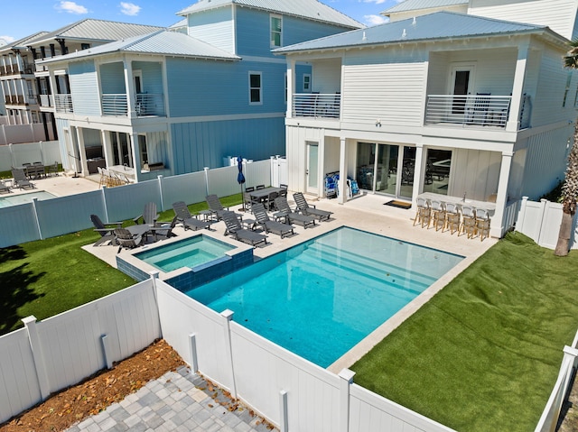 rear view of property featuring a balcony, exterior bar, a pool with hot tub, and a patio area