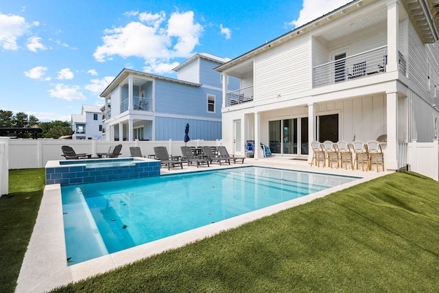 rear view of property featuring a balcony, a patio area, a swimming pool with hot tub, and a lawn