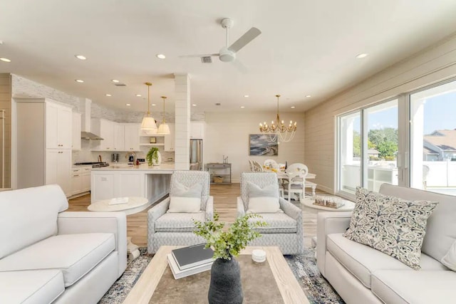 living room with ceiling fan with notable chandelier and light hardwood / wood-style floors