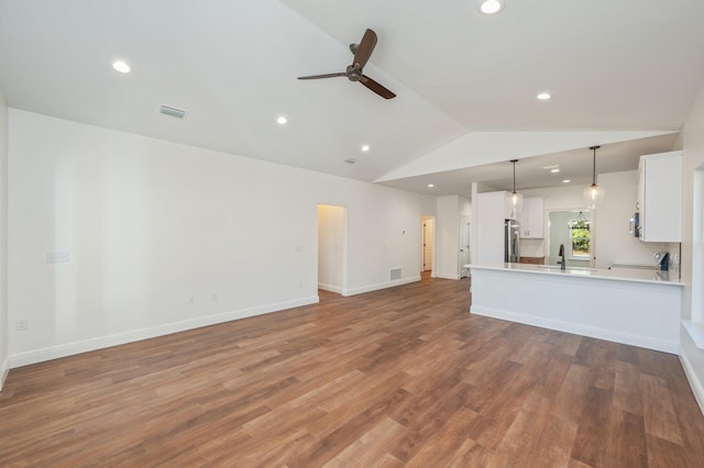 unfurnished living room with ceiling fan, sink, hardwood / wood-style floors, and vaulted ceiling