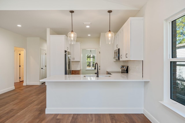 kitchen with pendant lighting, kitchen peninsula, decorative backsplash, white cabinetry, and appliances with stainless steel finishes