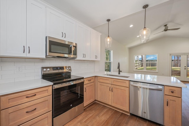 kitchen with kitchen peninsula, appliances with stainless steel finishes, hanging light fixtures, vaulted ceiling, and sink