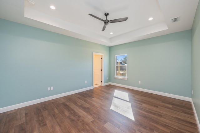 spare room featuring ceiling fan, dark wood-type flooring, and a raised ceiling