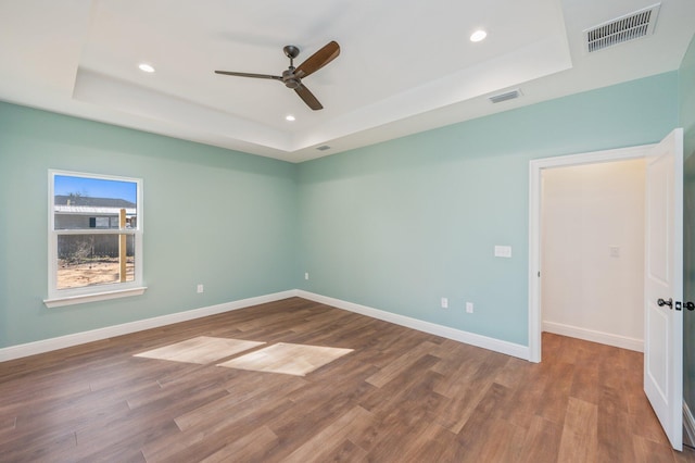 empty room featuring ceiling fan, hardwood / wood-style flooring, and a tray ceiling