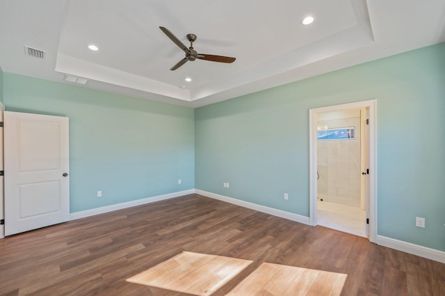 unfurnished bedroom with ceiling fan, a tray ceiling, dark hardwood / wood-style flooring, and ensuite bathroom