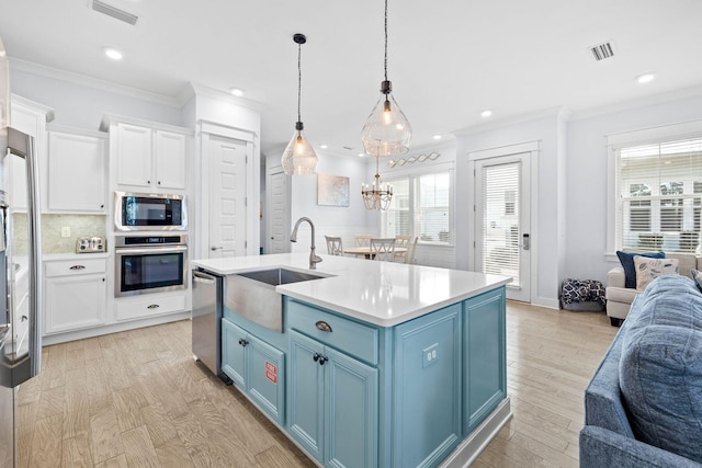 kitchen with blue cabinets, decorative light fixtures, white cabinets, a kitchen island with sink, and appliances with stainless steel finishes