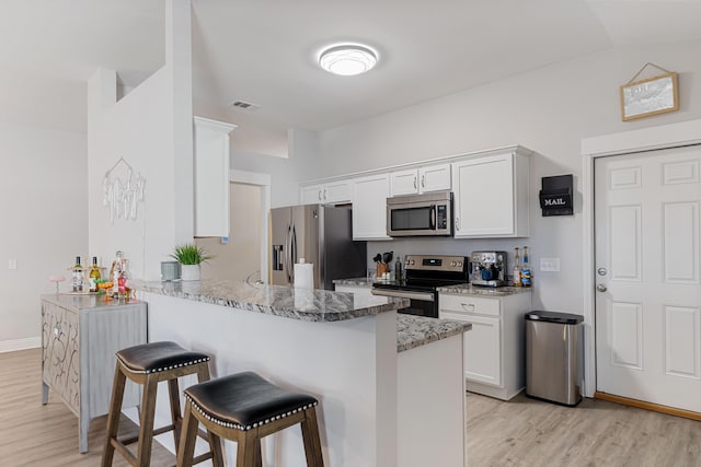 kitchen featuring visible vents, white cabinets, a peninsula, stainless steel appliances, and a kitchen bar