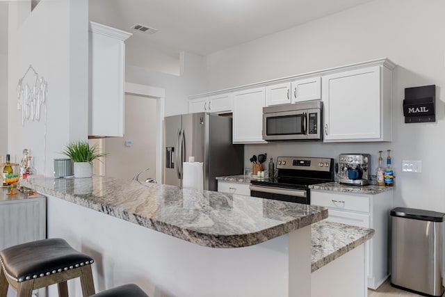 kitchen with a peninsula, visible vents, white cabinetry, a kitchen breakfast bar, and appliances with stainless steel finishes