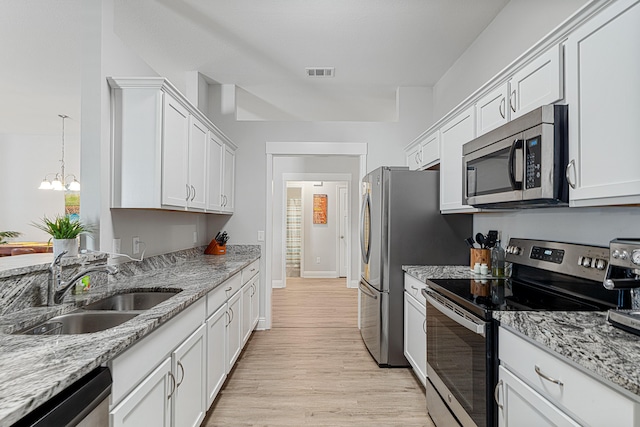 kitchen featuring stainless steel appliances, white cabinetry, a sink, light stone countertops, and light wood-type flooring