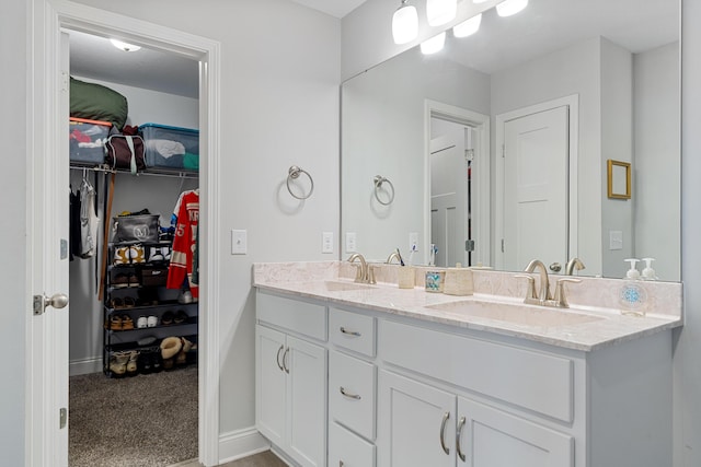 bathroom featuring a spacious closet, double vanity, a sink, and baseboards