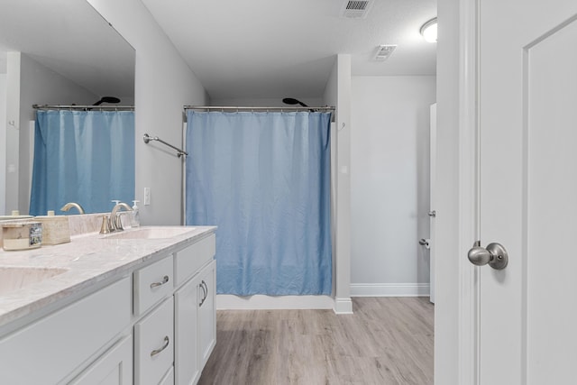 bathroom featuring double vanity, visible vents, a sink, and wood finished floors