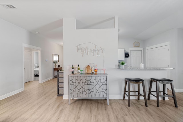 kitchen featuring light wood finished floors, white cabinets, a peninsula, vaulted ceiling, and light countertops