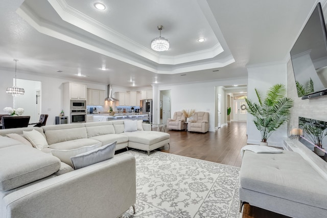 living room featuring a raised ceiling, ornamental molding, a chandelier, and hardwood / wood-style floors