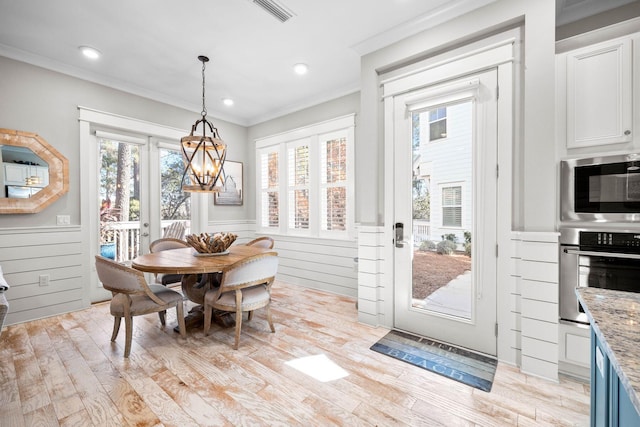 dining area with light hardwood / wood-style flooring, an inviting chandelier, crown molding, and wood walls