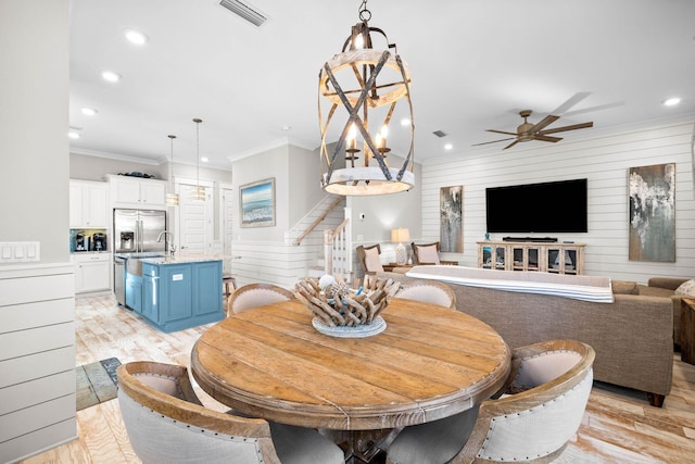 dining room featuring ceiling fan with notable chandelier, wood walls, crown molding, and light hardwood / wood-style flooring