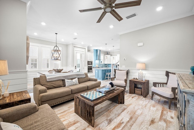 living room with light wood-type flooring, ceiling fan, and ornamental molding