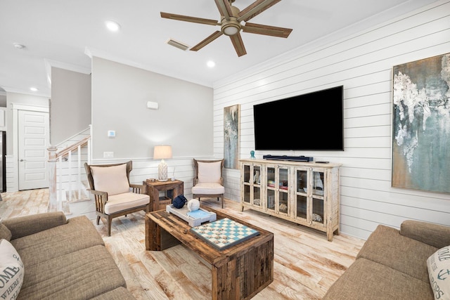 living room with light wood-type flooring, ceiling fan, crown molding, and wooden walls