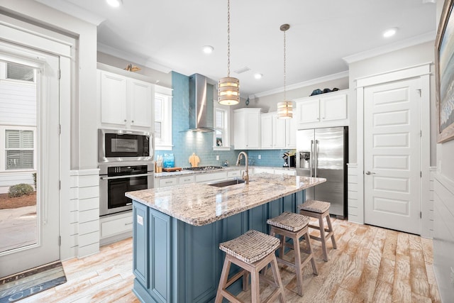 kitchen featuring wall chimney exhaust hood, hanging light fixtures, a kitchen island with sink, appliances with stainless steel finishes, and sink