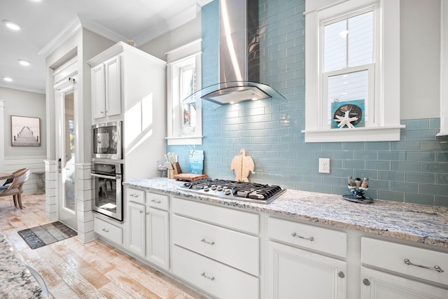 kitchen with stainless steel appliances, white cabinets, ornamental molding, and wall chimney exhaust hood