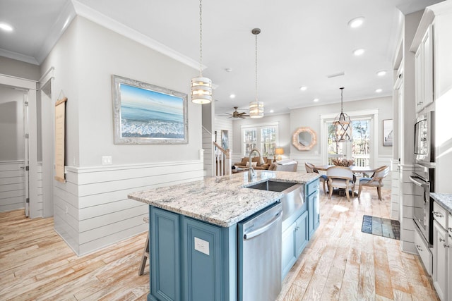 kitchen with a center island with sink, stainless steel appliances, ceiling fan, white cabinetry, and blue cabinets