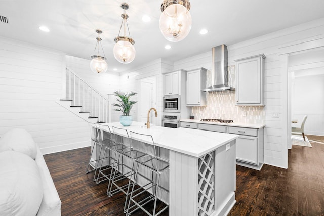 kitchen featuring decorative light fixtures, an island with sink, a breakfast bar area, stainless steel appliances, and wall chimney range hood