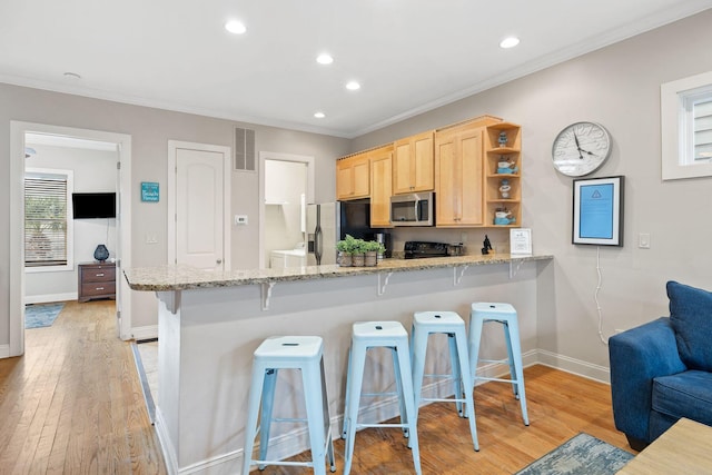 kitchen with appliances with stainless steel finishes, kitchen peninsula, a breakfast bar, light brown cabinets, and light hardwood / wood-style flooring