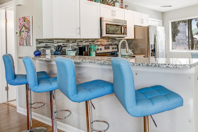 kitchen featuring tasteful backsplash, a breakfast bar area, white cabinetry, and appliances with stainless steel finishes