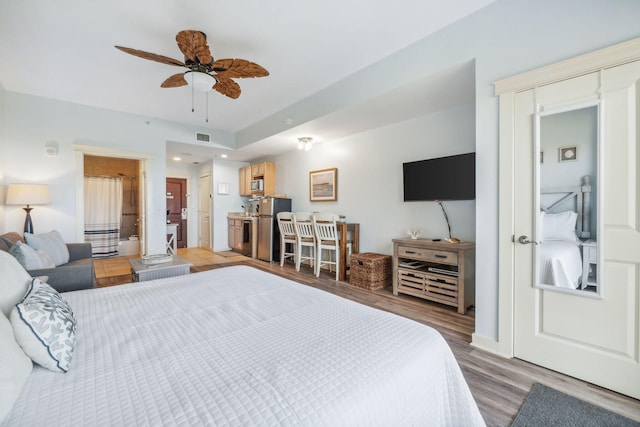 bedroom with ceiling fan, stainless steel fridge, light wood-type flooring, and ensuite bath