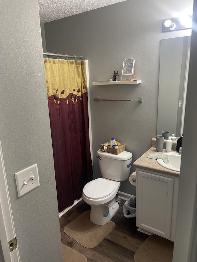 bathroom featuring toilet, vanity, hardwood / wood-style flooring, a textured ceiling, and curtained shower