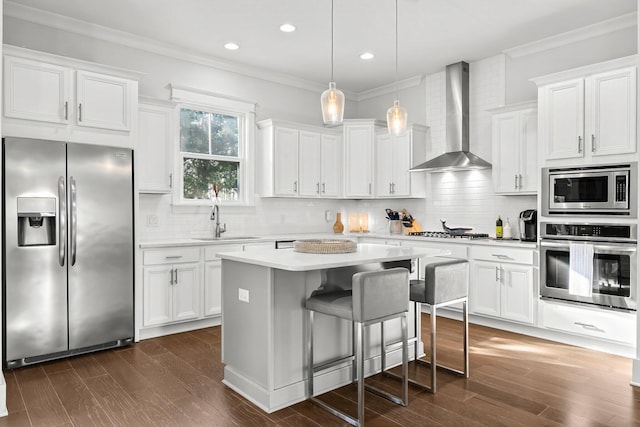 kitchen with pendant lighting, white cabinetry, wall chimney range hood, stainless steel appliances, and sink